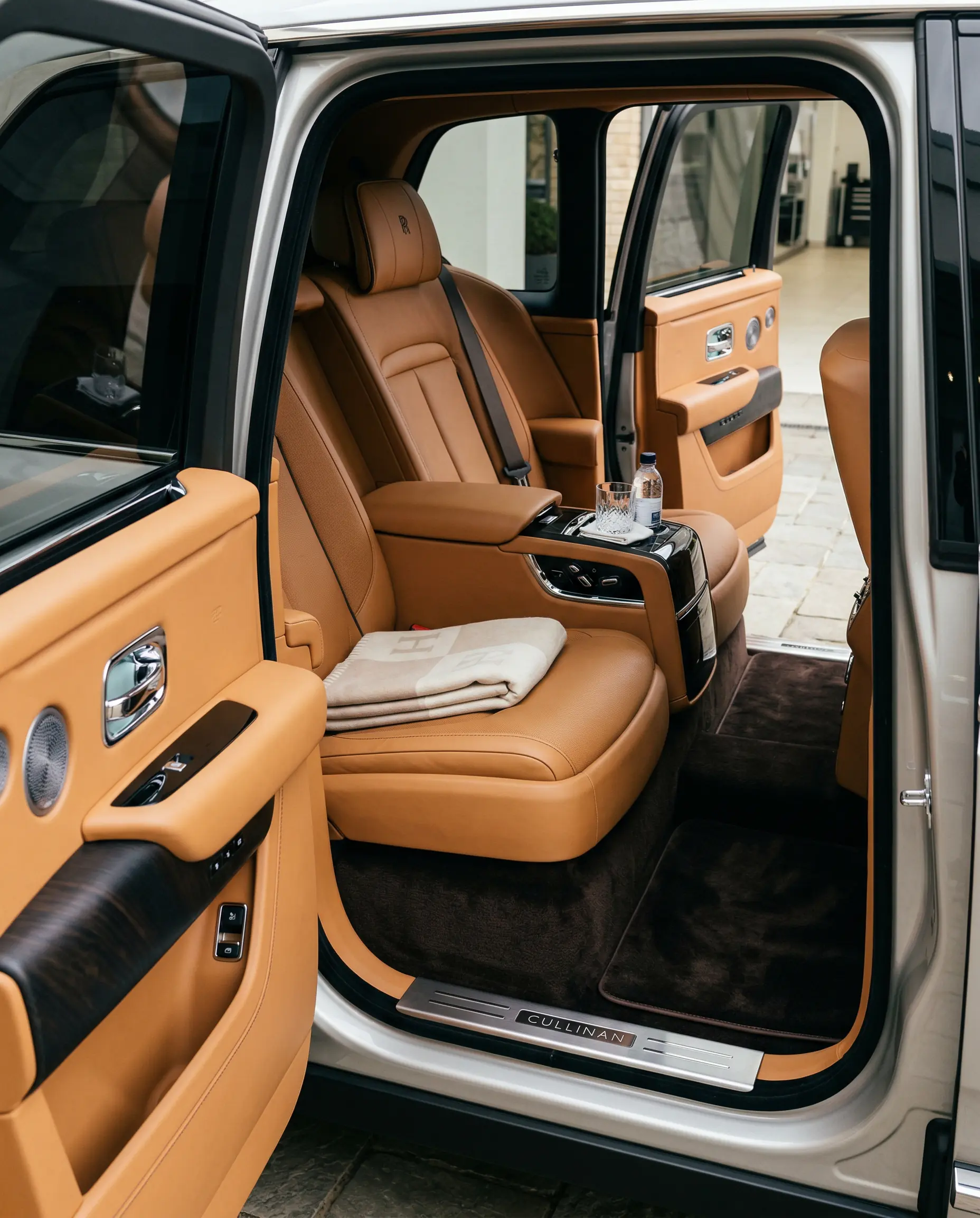 Rolls-Royce Cullinan rear cabin with tan leather seats, crystal glassware, and a folded cashmere throw